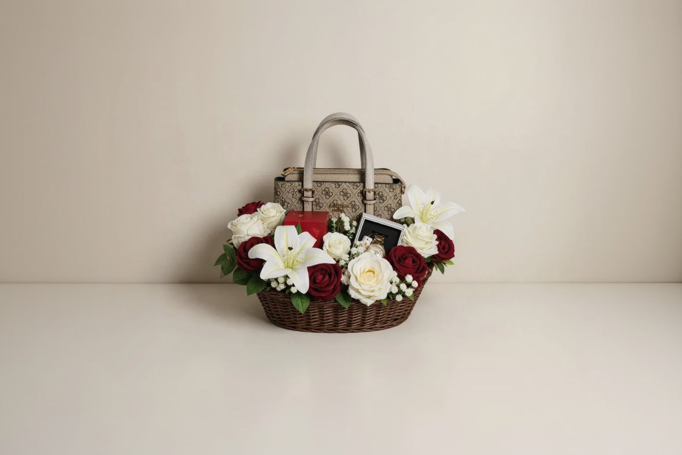 A luxury gift basket featuring a brown wicker basket filled with red and white roses, white lilies, and baby's breath, with a beige patterned Gucci handbag and a red box inside.