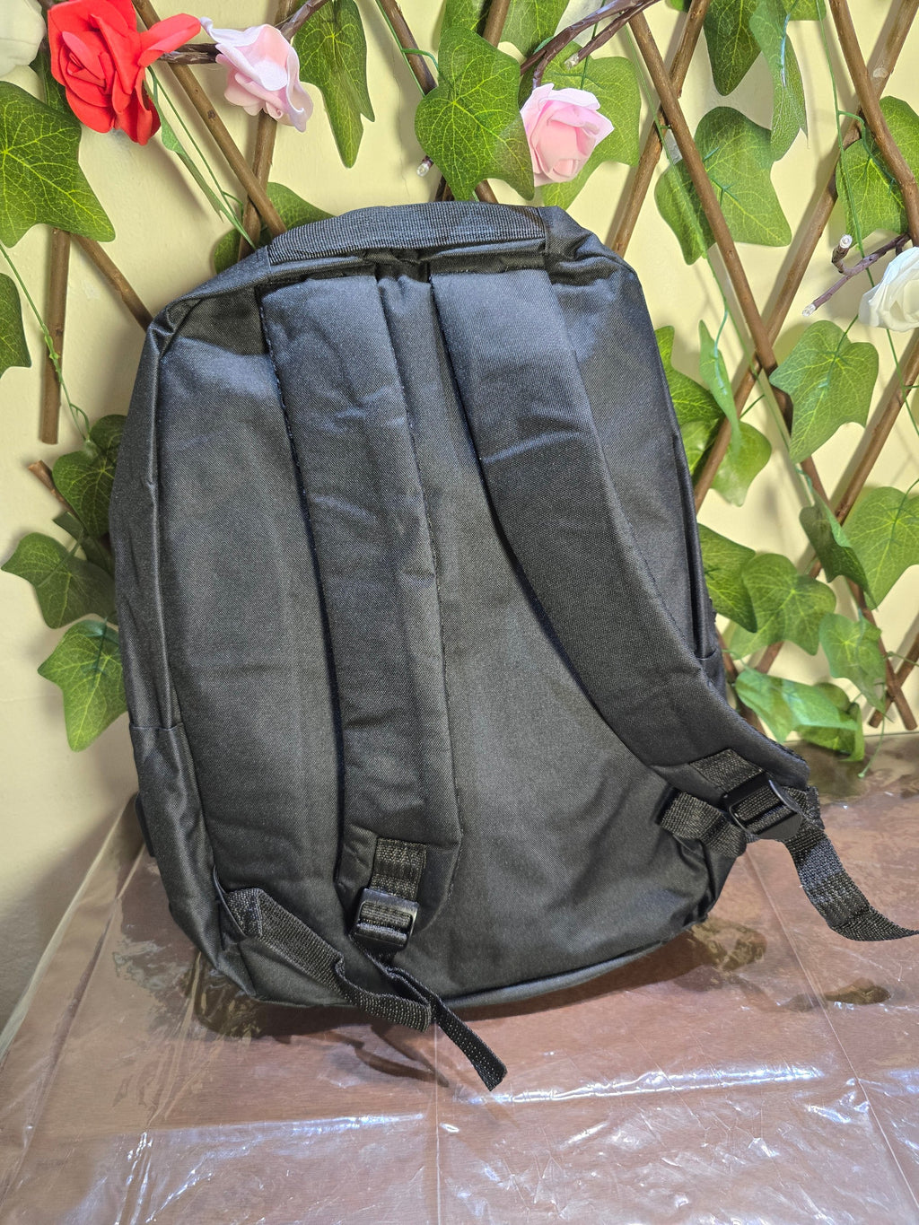BioCode black minimalist laptop backpack with padded adjustable shoulder straps against a decorative floral background