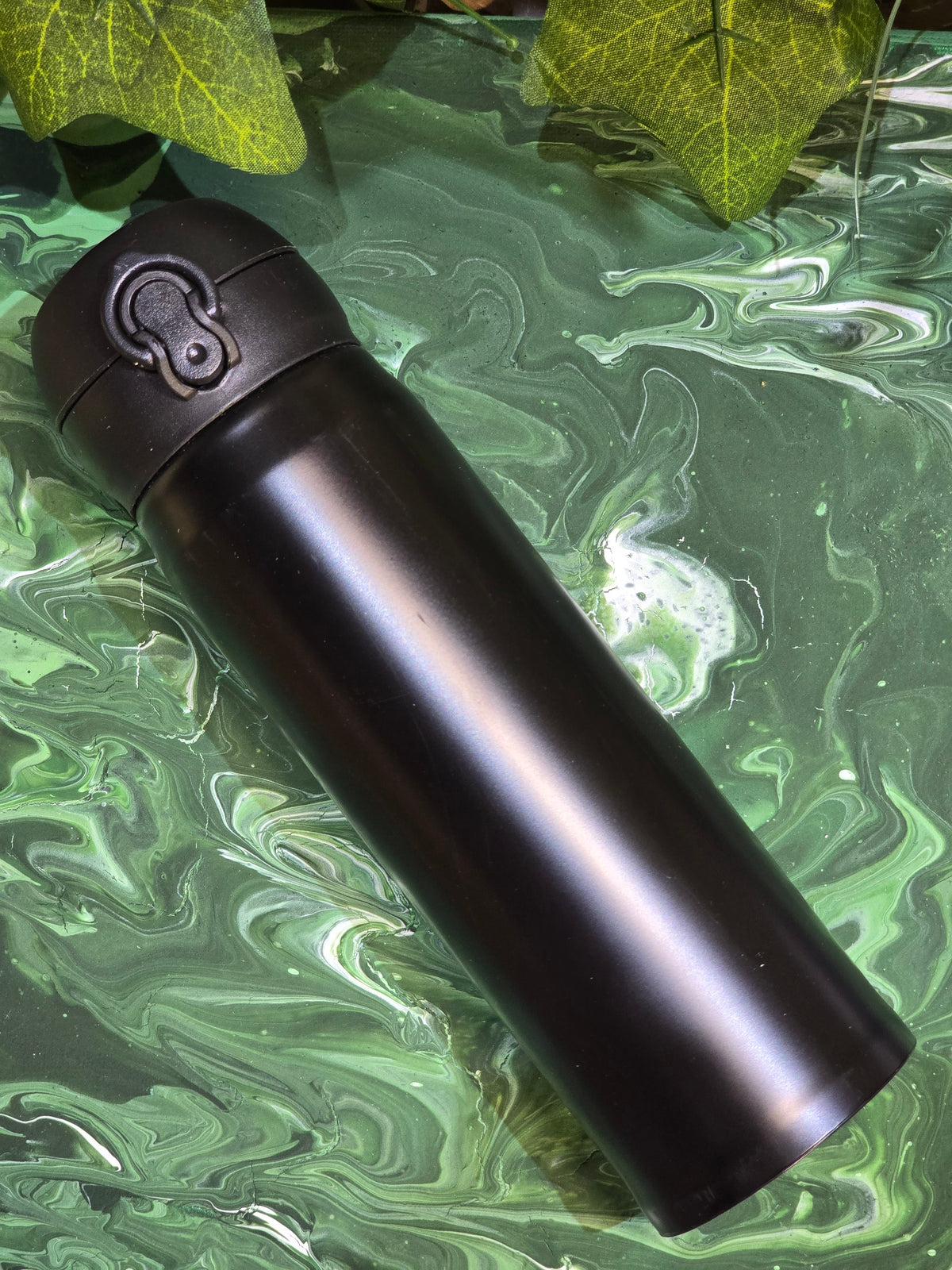 BioCode insulated stainless steel travel flask in matte black with a leak-proof flip-top lid on a green marble surface