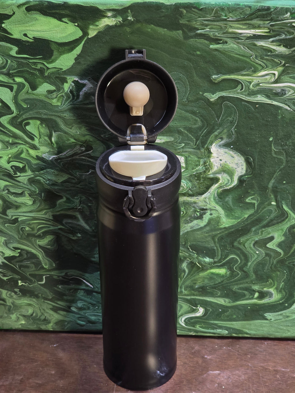 BioCode black stainless steel vacuum insulated travel flask with open leak-proof flip-top lid against green background