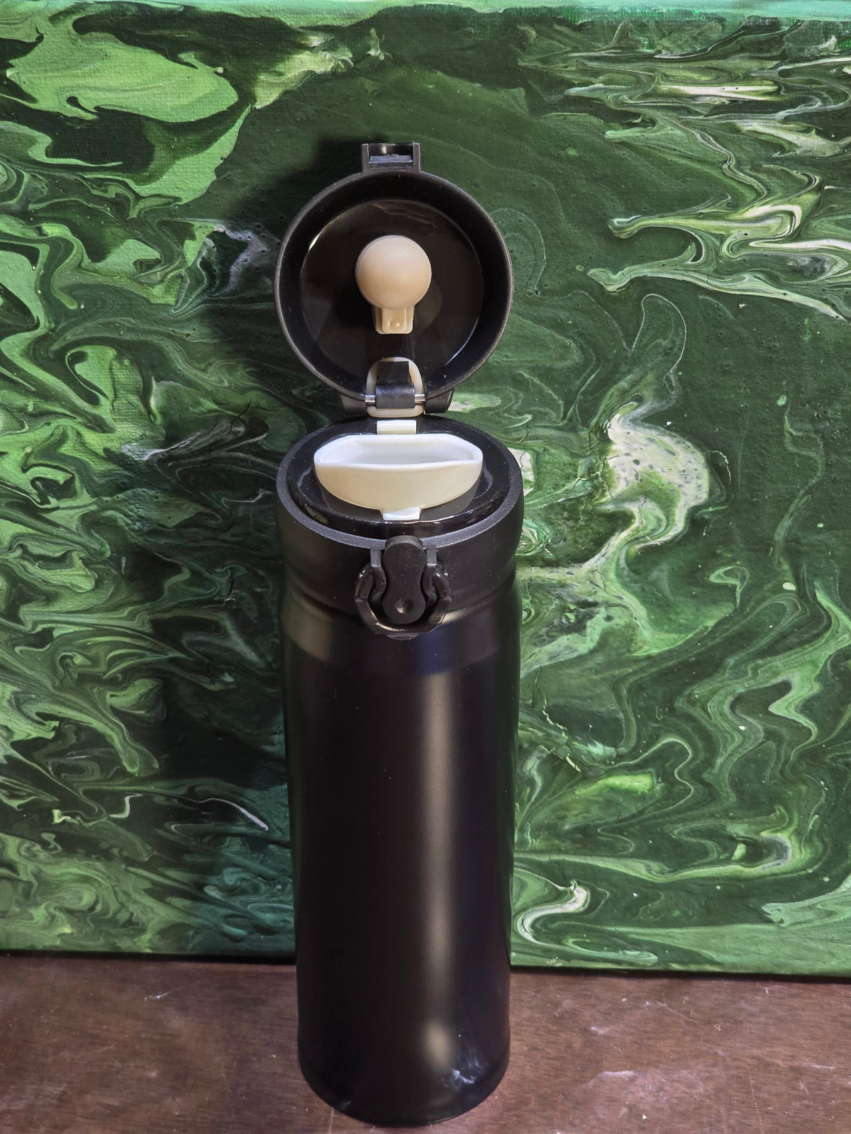 BioCode black stainless steel vacuum insulated travel flask with open leak-proof flip-top lid against green background
