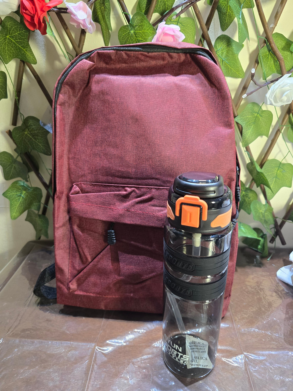 BioCode burgundy textured backpack and clear sports water bottle with black and orange lid and straw