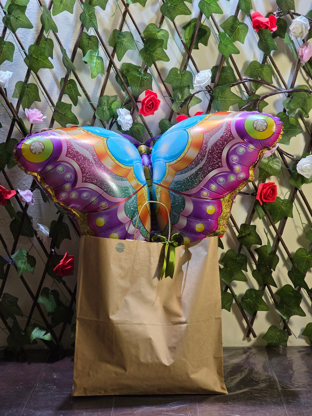 BioCode gift set featuring a large colourful butterfly balloon emerging from a brown paper bag against a floral trellis