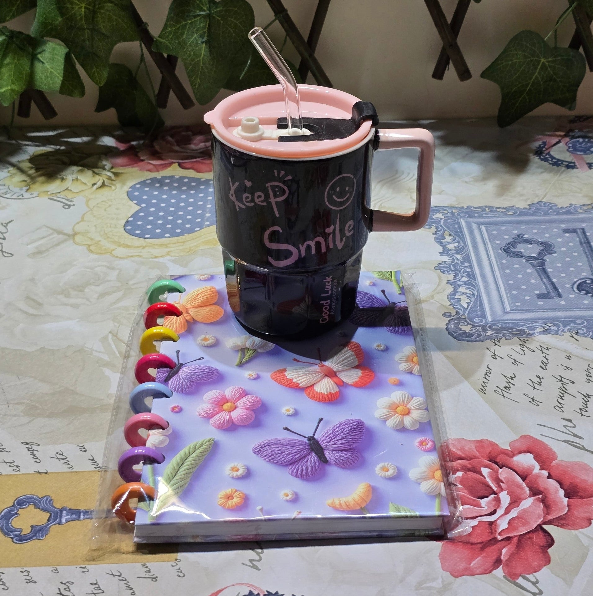 BioCode stationery set featuring a butterfly discbound notebook and a black Keep Smile mug with a pink lid and straw.