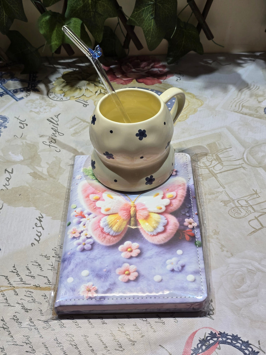 BioCode decorative notebook with a 3D butterfly design, cream ceramic mug with blue flowers, and a glass straw.