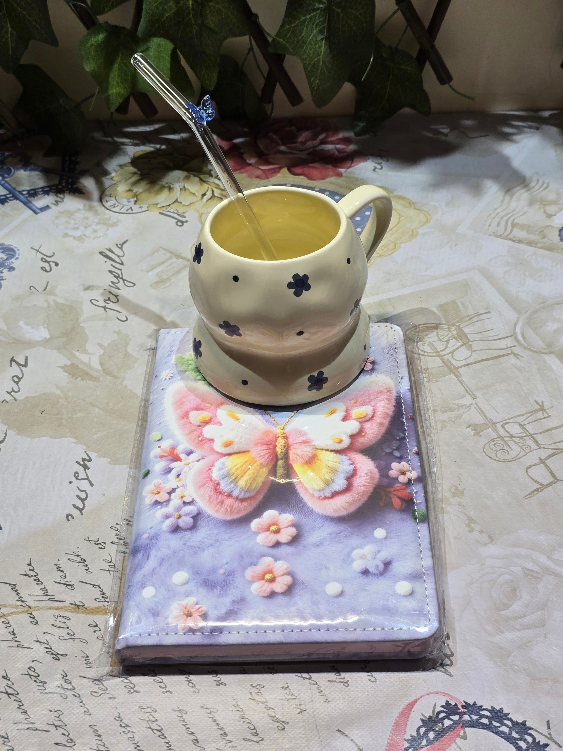 BioCode decorative notebook with a 3D butterfly design, cream ceramic mug with blue flowers, and a glass straw.