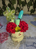 BioCode cream ceramic pot with red cherry print, filled with makeup brushes, lipstick, and decorative red flowers.