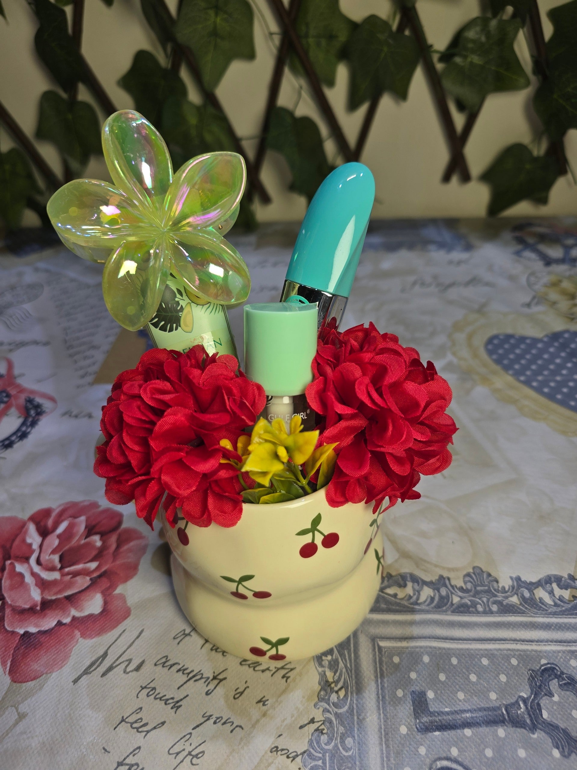 BioCode cream ceramic pot with red cherry print, filled with makeup brushes, lipstick, and decorative red flowers.