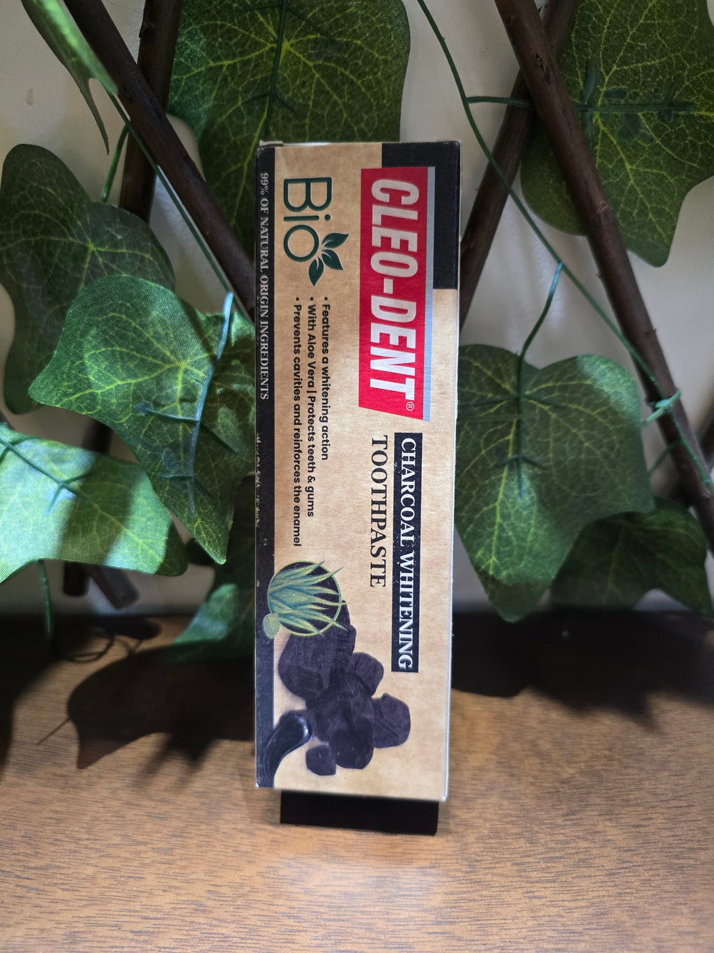 BioCode Cleo-Dent charcoal whitening toothpaste box with natural ingredients, set against a decorative leaf backdrop.