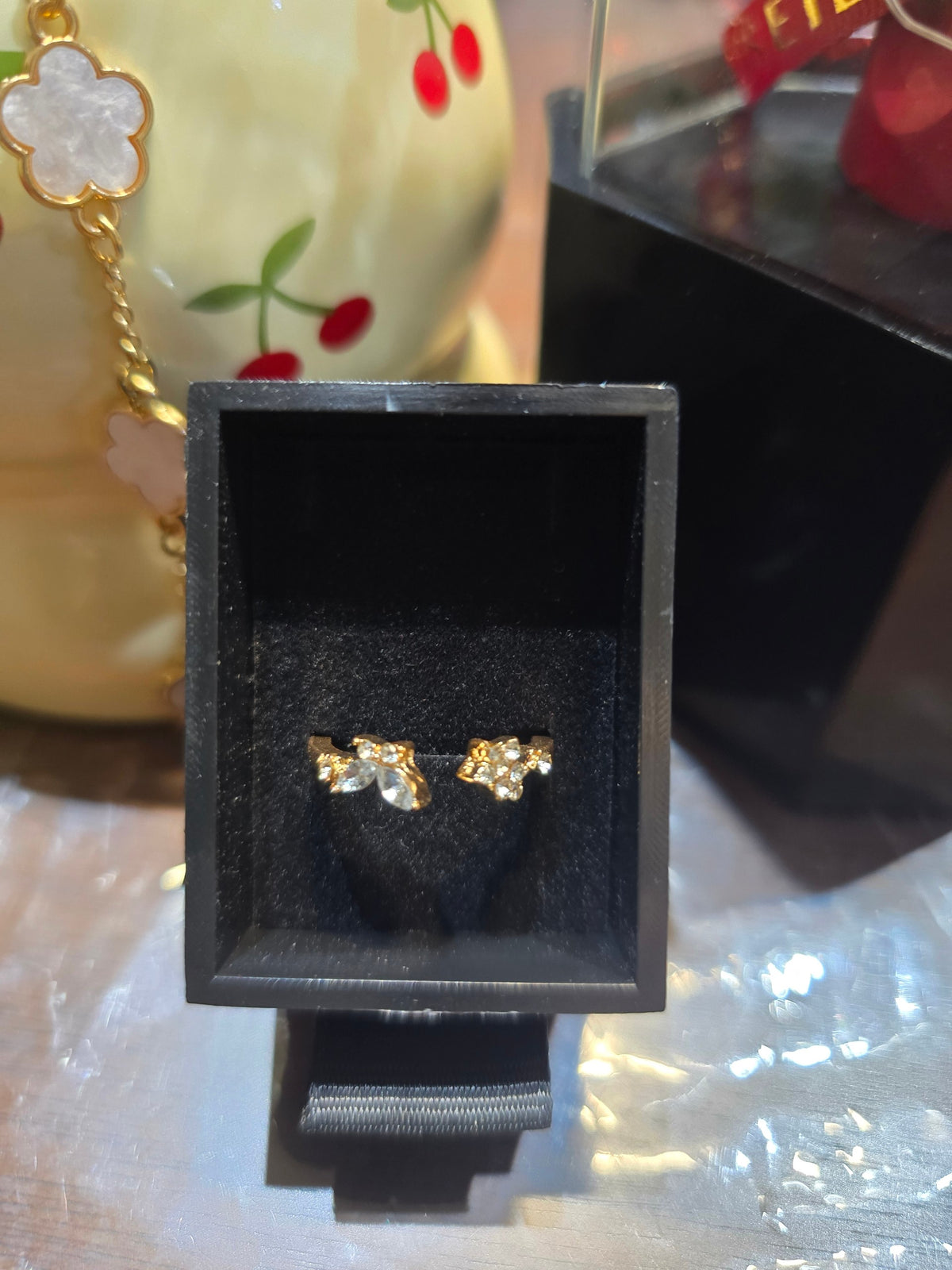 BioCode crystal-encrusted gold-toned earrings displayed in a black velvet jewellery box with a cherry mug background