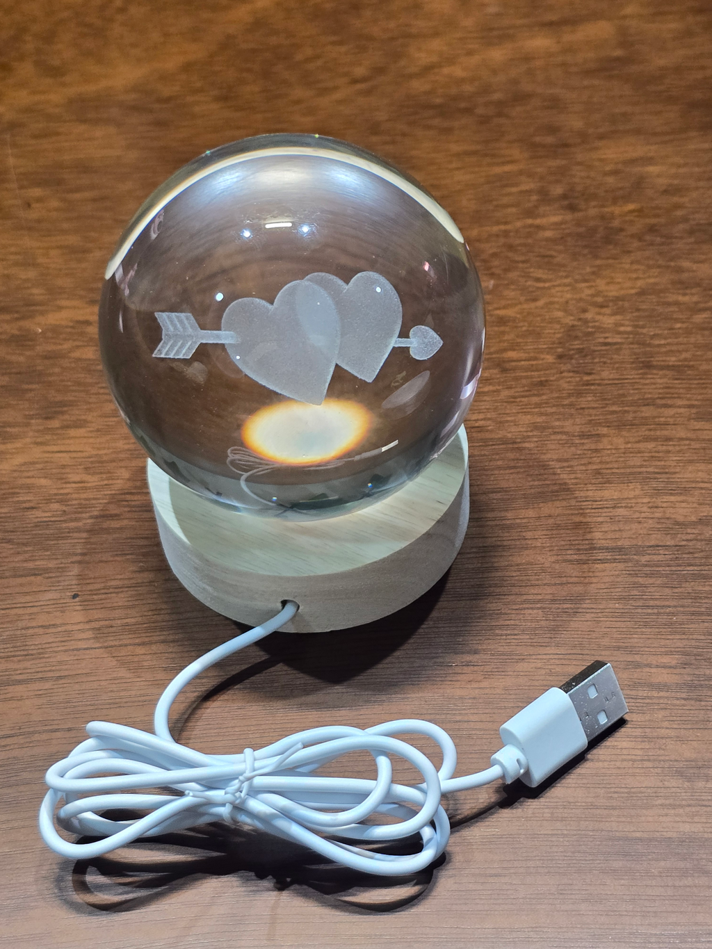 BioCode crystal ball with laser-engraved hearts and arrow on a wooden LED base with a white USB power cable