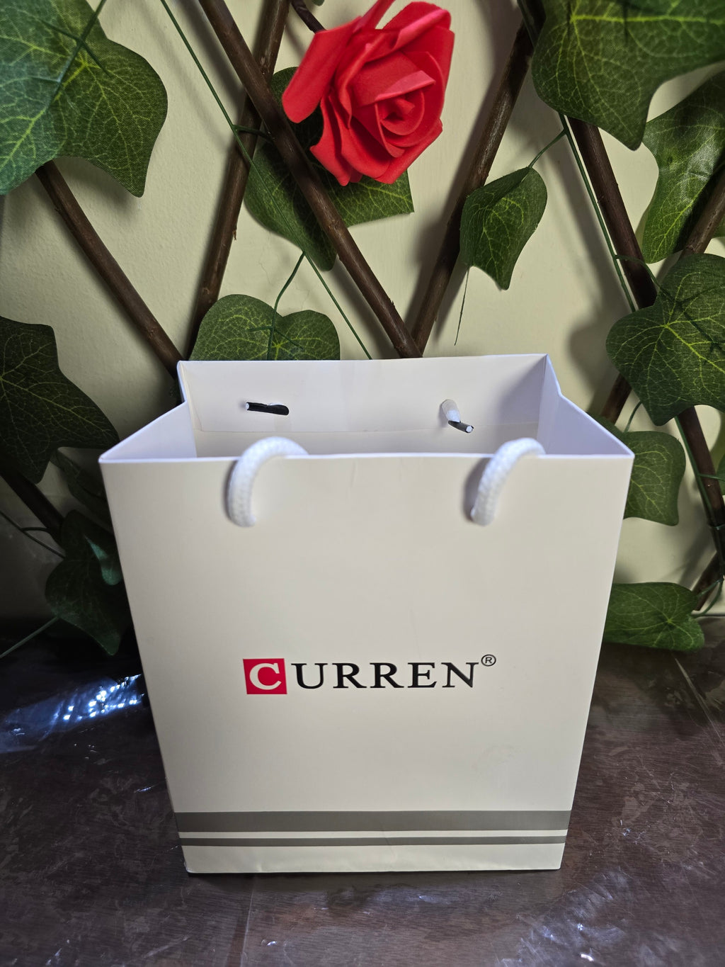 BioCode white branded gift bag for CURREN watch set, featuring a red rose and green foliage background.