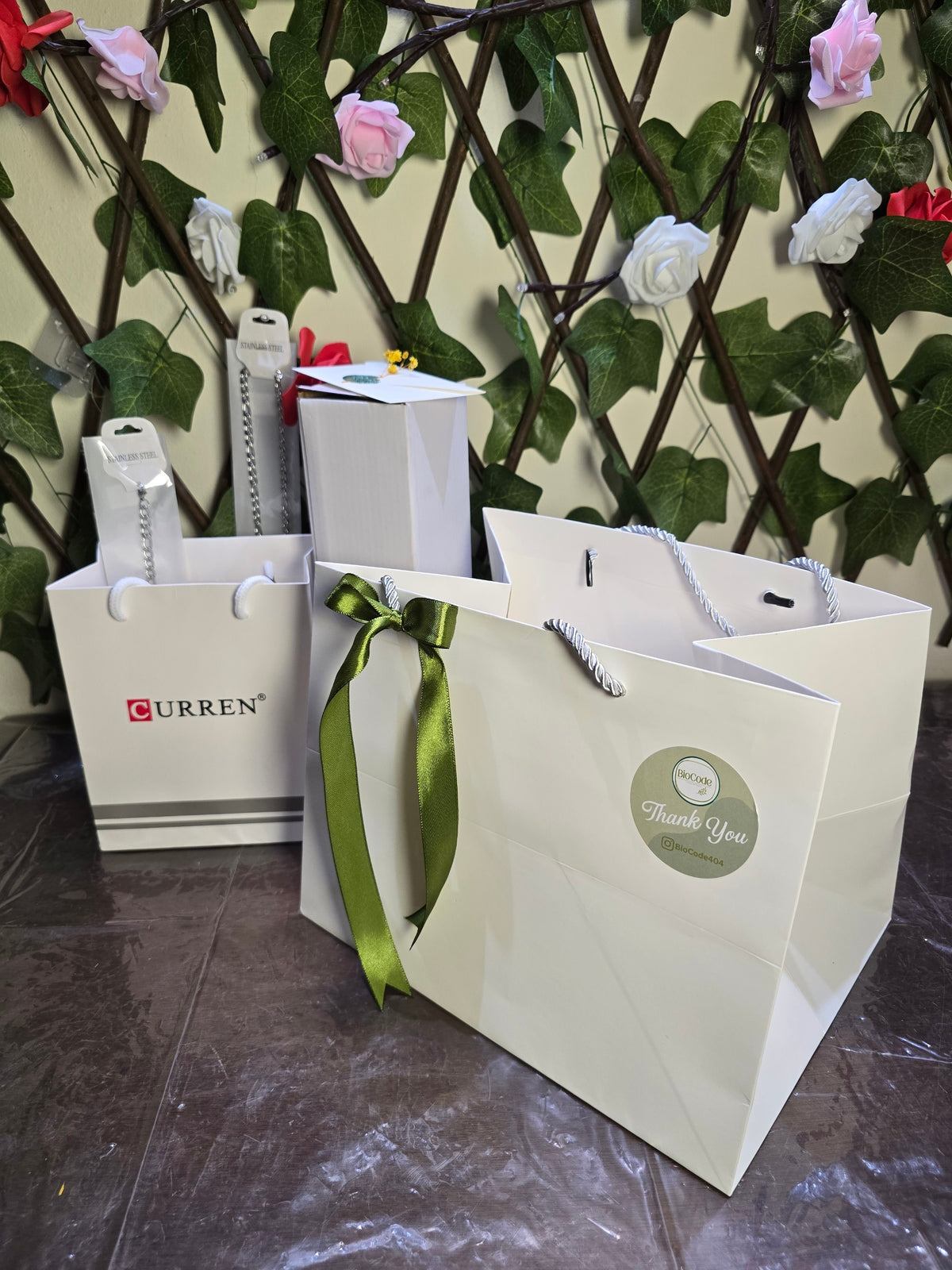 BioCode gift bags and packaging for CURREN watch and accessories set with green ribbon against a floral trellis