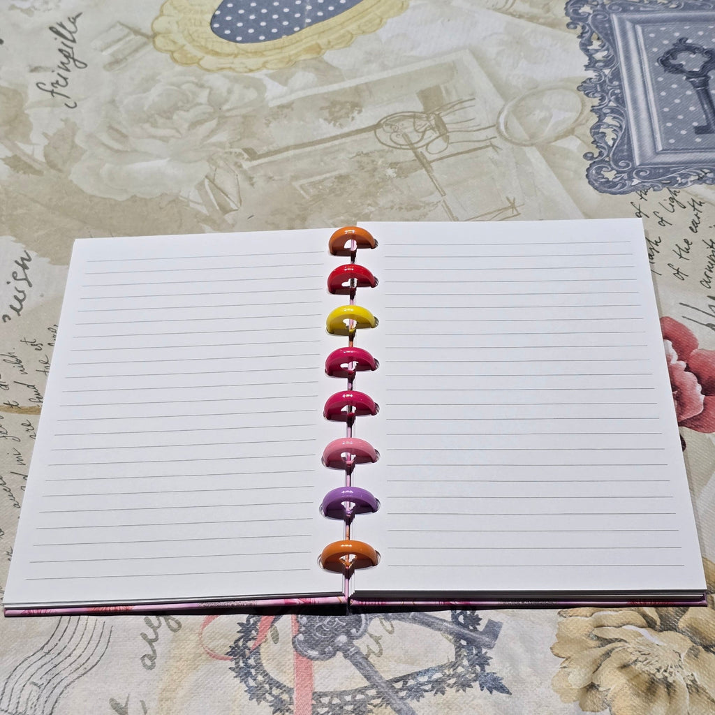 BioCode discbound notebook open to lined pages with colourful rainbow discs on a vintage floral patterned background