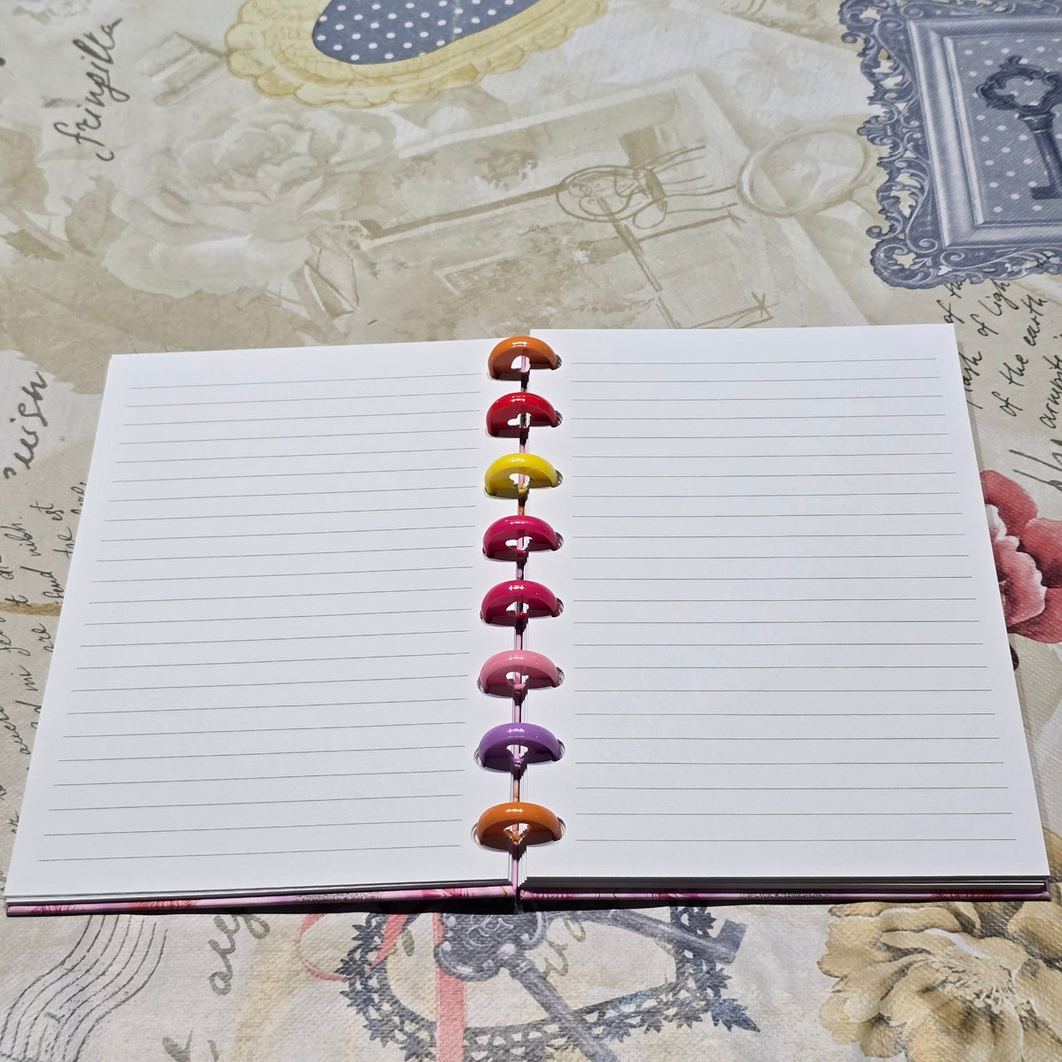 BioCode discbound notebook open to lined pages with colourful rainbow discs on a vintage floral patterned background