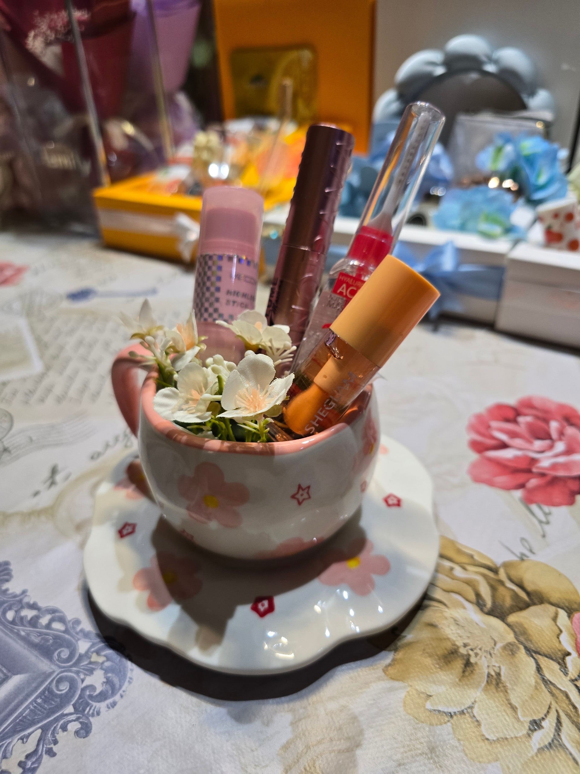 BioCode ceramic teacup and saucer with pink floral motifs and star accents holding makeup brushes and lip glosses