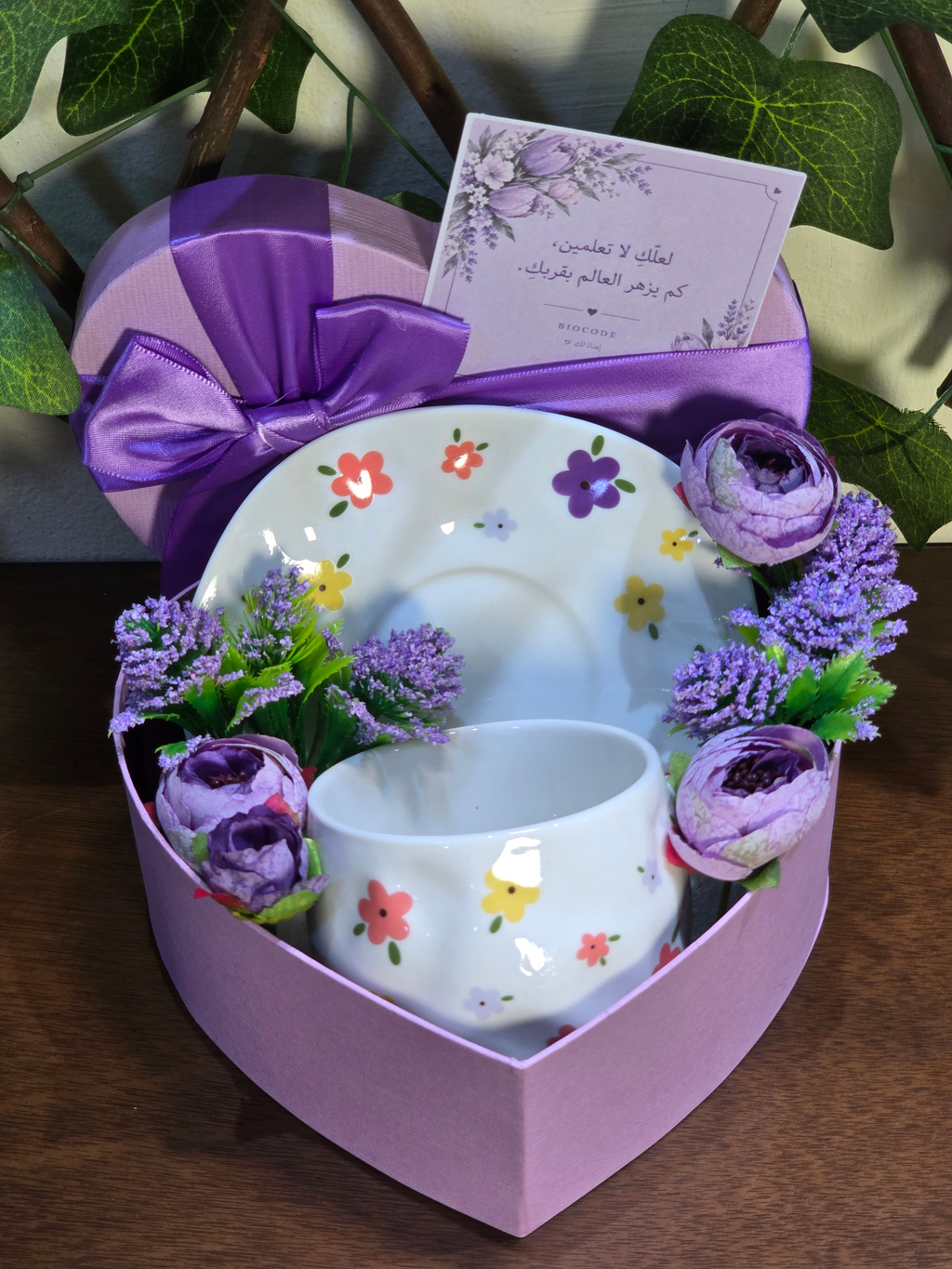 BioCode floral ceramic tea cup and saucer set in a heart-shaped purple gift box with artificial flowers and a note.