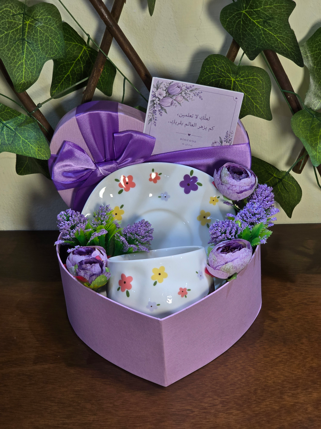 BioCode floral ceramic tea cup and saucer set in a heart-shaped purple gift box with artificial flowers and a note.