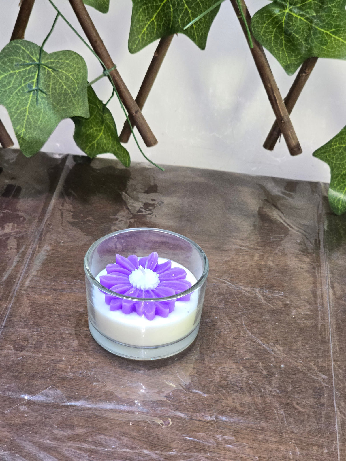 BioCode floral scented candle in a glass jar with a decorative purple flower wax topper on a wooden surface