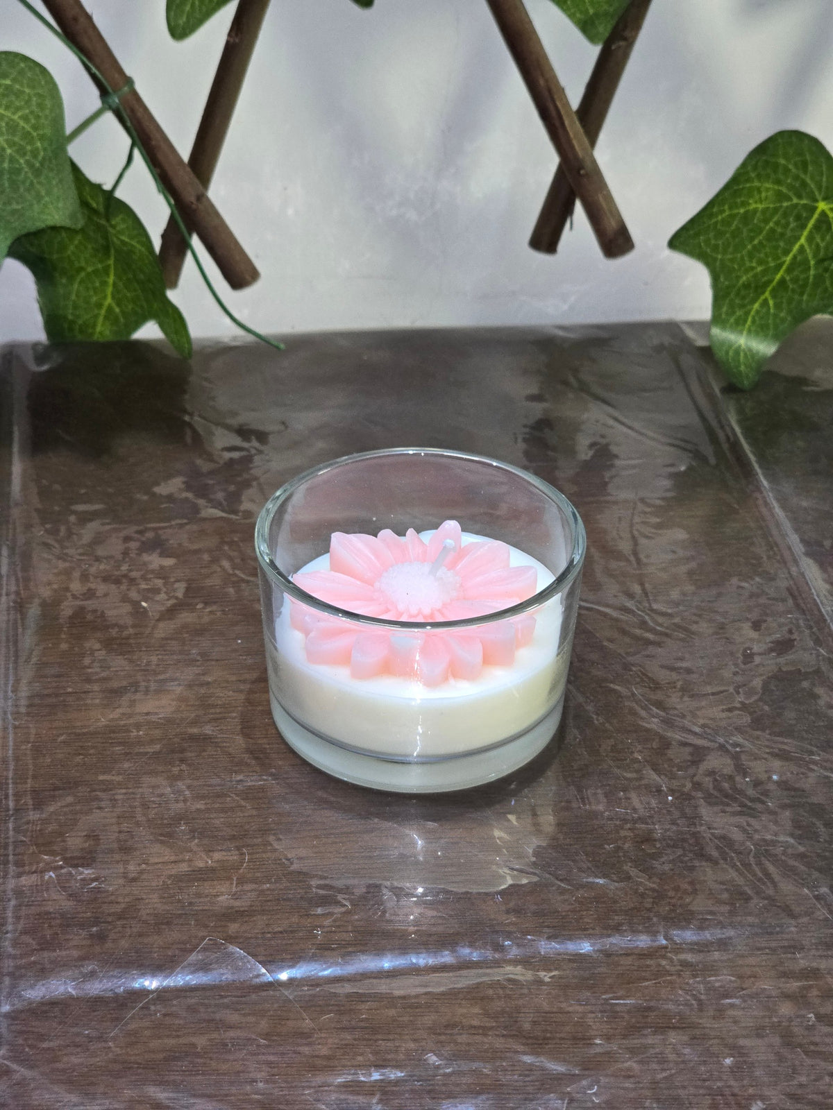 BioCode floral-scented candle in a glass jar with a decorative pink flower wax topper on a dark wooden surface