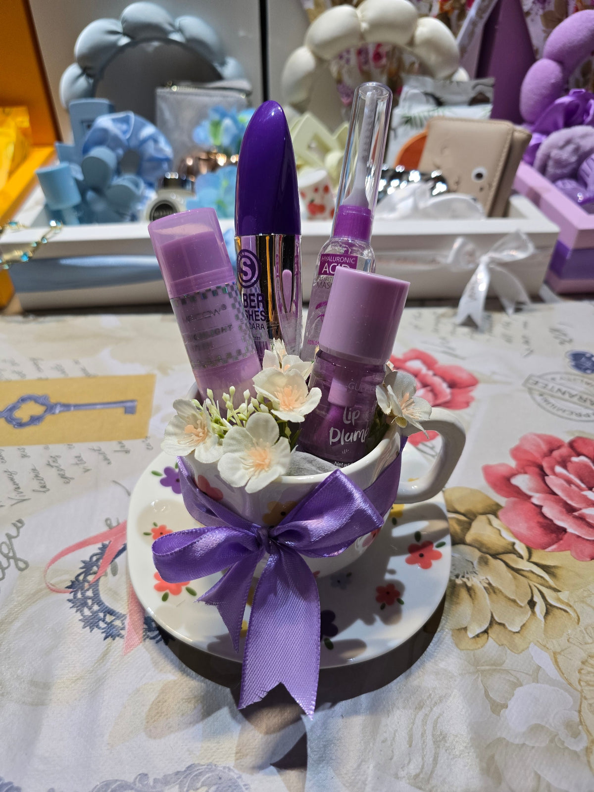 BioCode beauty gift set featuring mascara and lip plumper in a floral ceramic teacup with a purple ribbon bow.