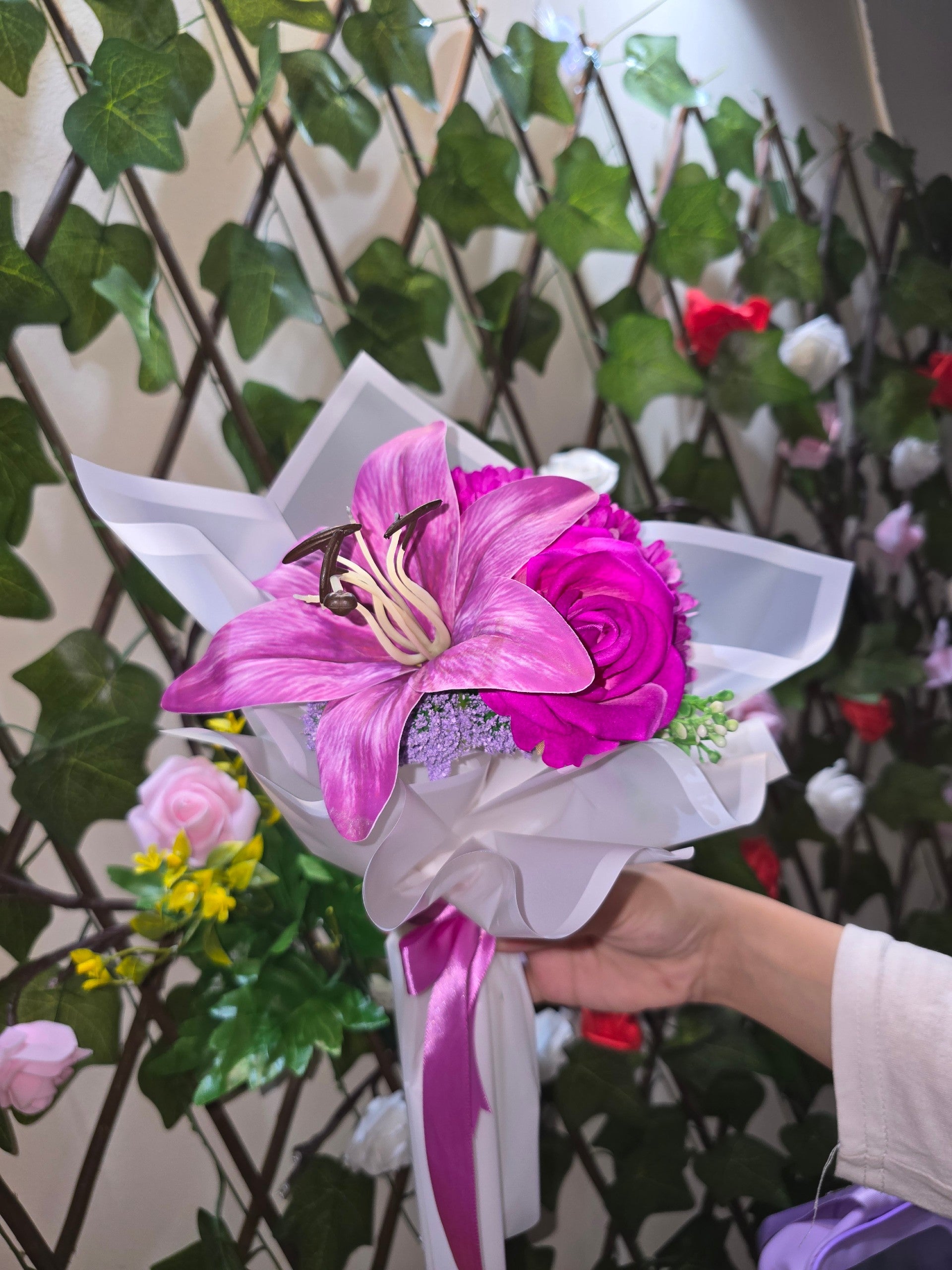 BioCode handcrafted artificial floral bouquet featuring a vibrant fuchsia lily and rose wrapped in white paper.