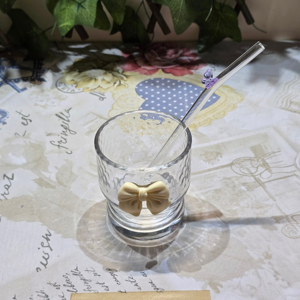BioCode decorative glass tumbler with cream bow and purple butterfly straw on a patterned table with a notebook