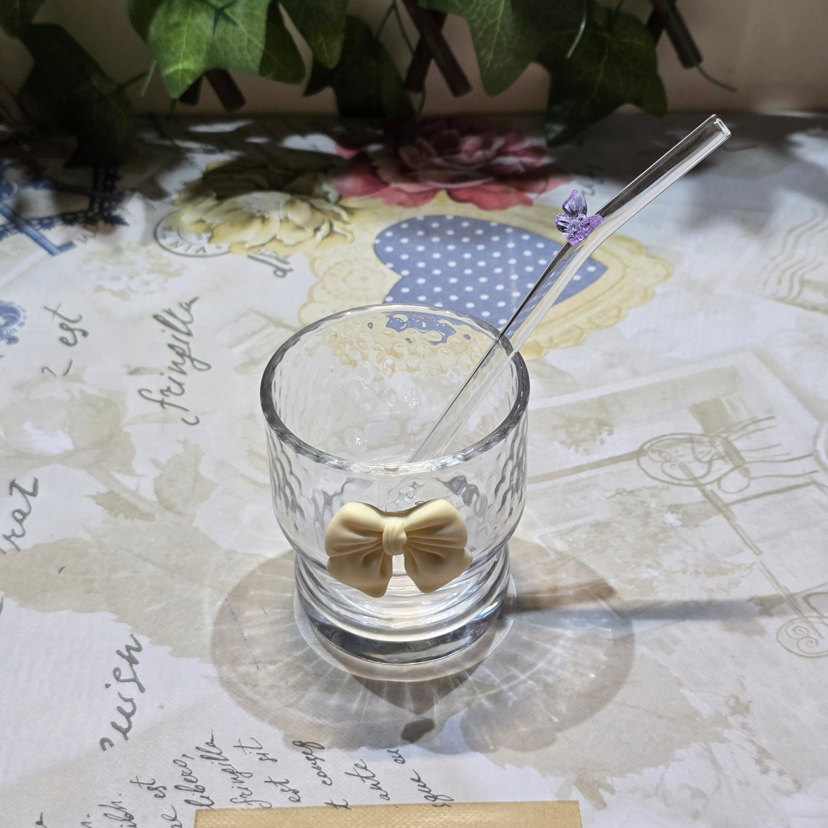 BioCode decorative glass tumbler with cream bow and purple butterfly straw on a patterned table with a notebook