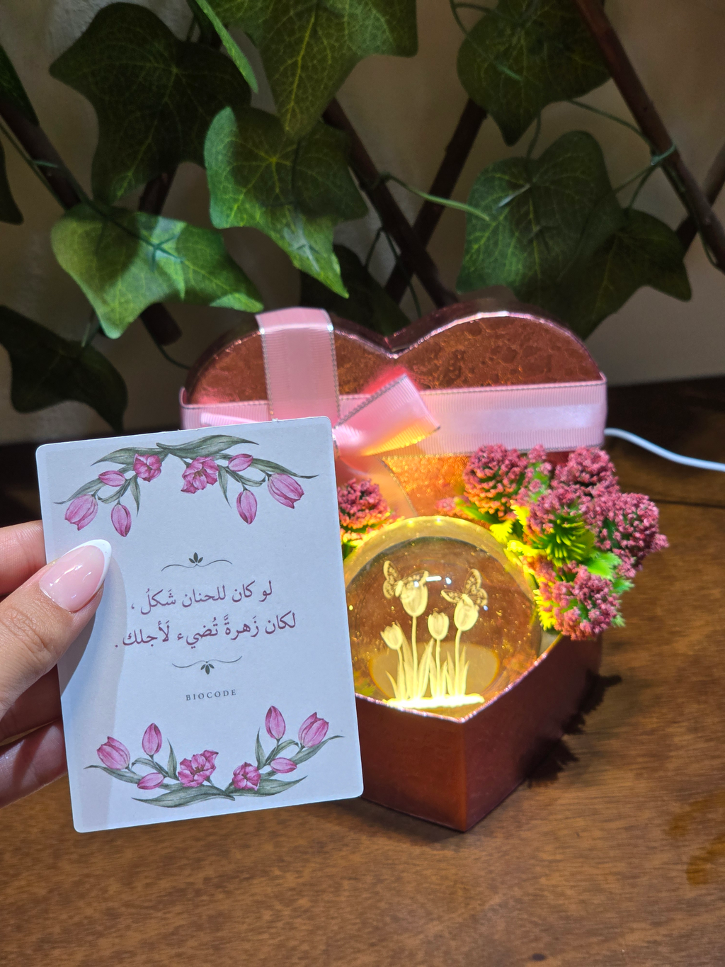 BioCode heart-shaped gift box with a glowing glass tulip sphere, pink ribbon, and floral accents with a greeting card.