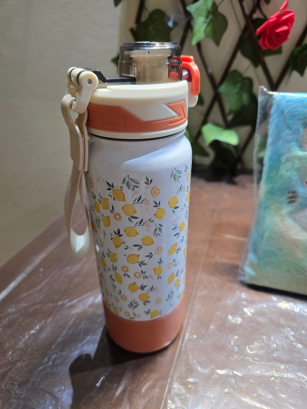 BioCode stainless steel water bottle with a lemon and leaf print, featuring an orange base and a secure carry strap.