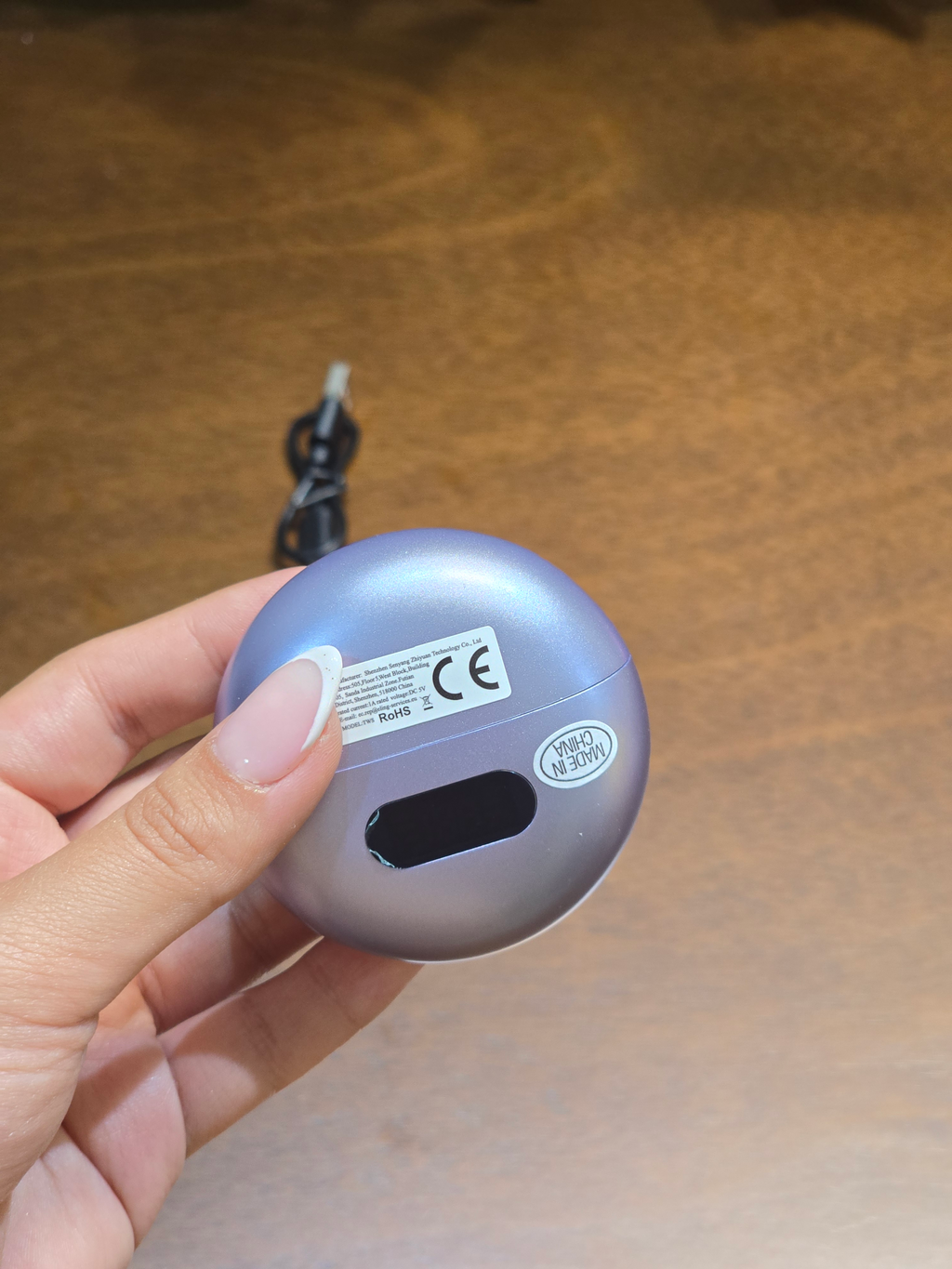 BioCode lilac wireless earbud charging case with digital display held in hand