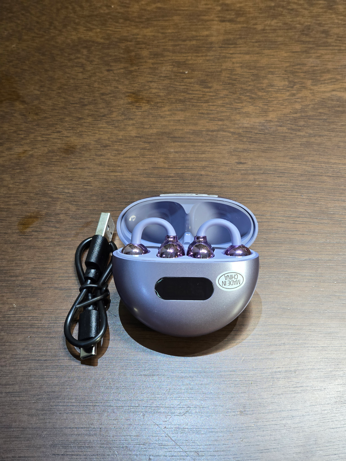 BioCode lilac wireless earbuds with metallic purple finish inside a rounded charging case with a digital display.