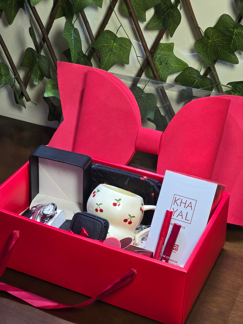 BioCode luxury gift hamper in a red box with a large bow, featuring a silver watch, cherry mug, and beauty items.