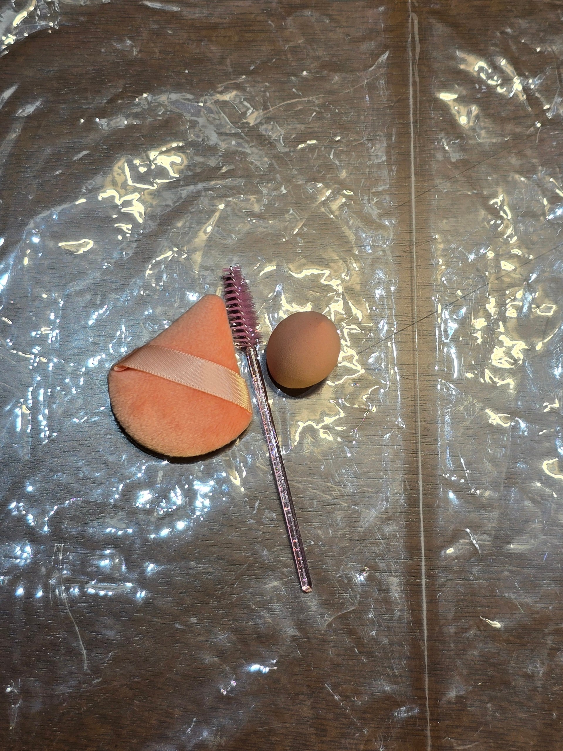 BioCode beauty set featuring a peach-coloured triangular powder puff, a pink spoolie brush, and a small makeup sponge.
