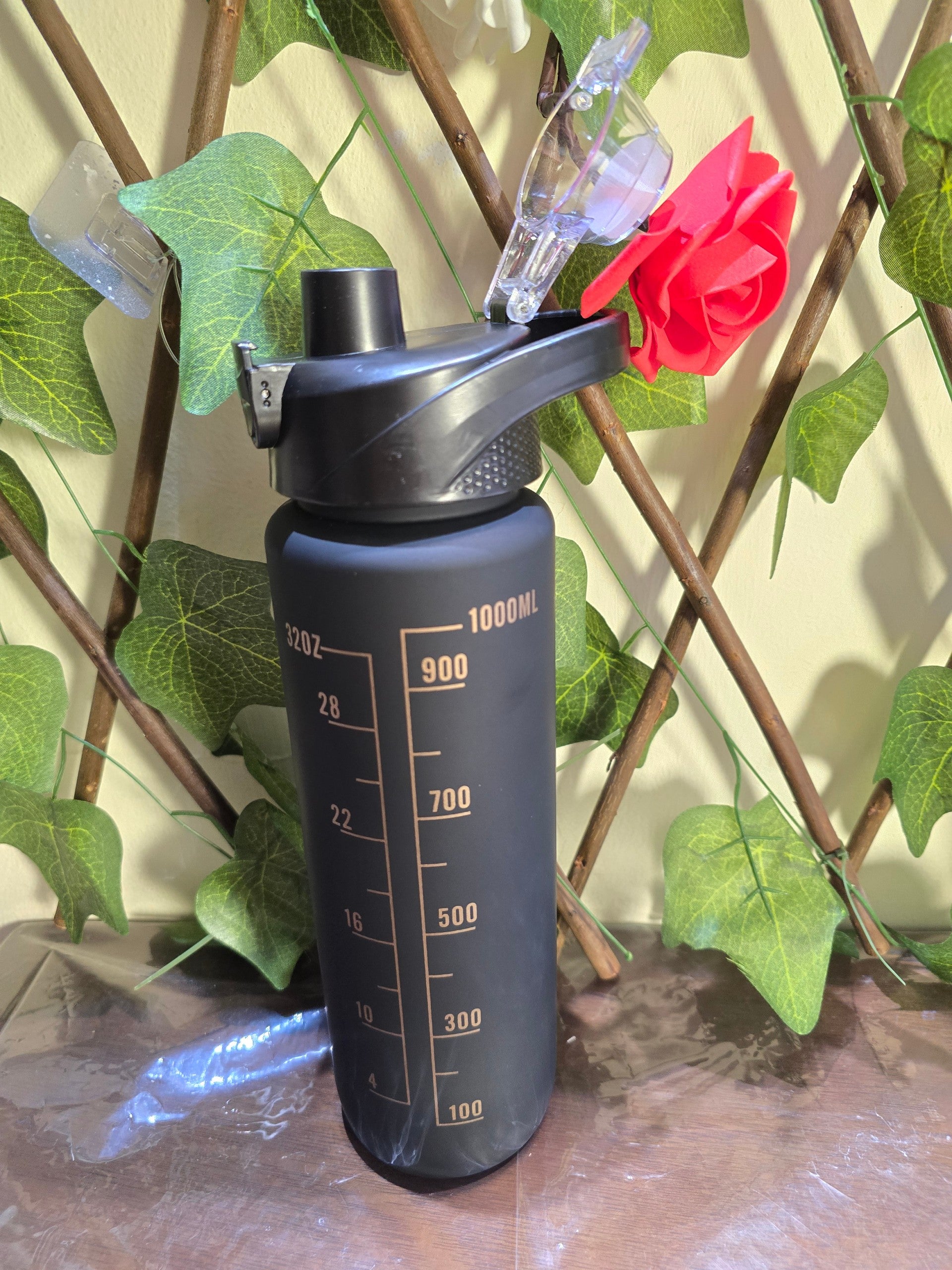 BioCode 1000ml matte black motivational water bottle with gold measurement markings and a flip-top lid