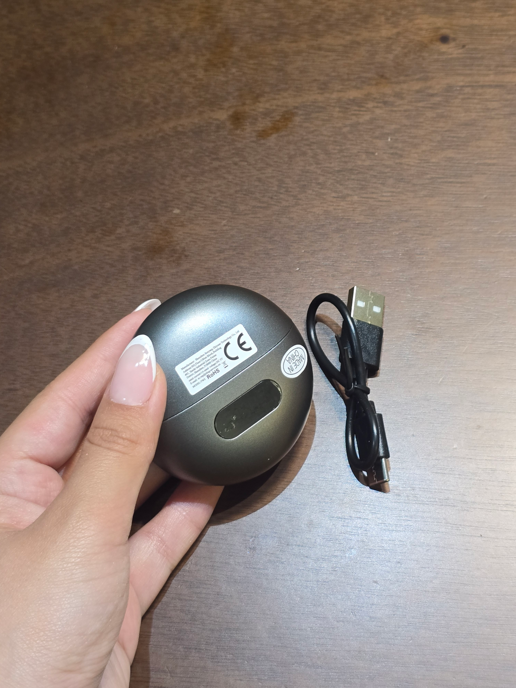 BioCode wireless earbuds in a metallic grey circular charging case held in a hand with a black USB charging cable.