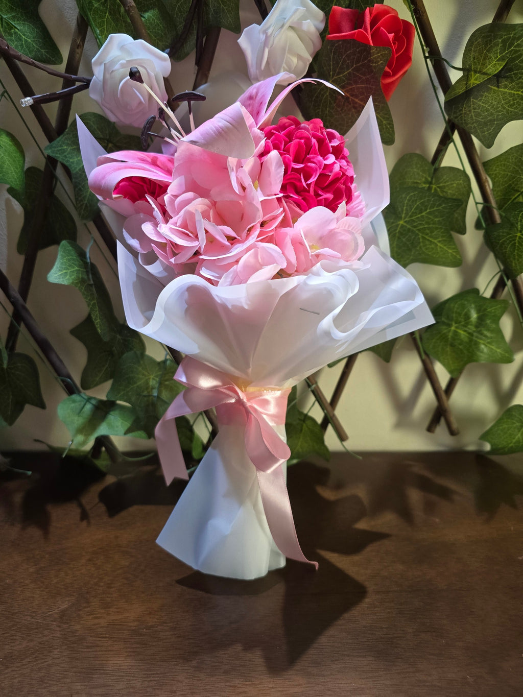 BioCode artificial pink lily and hydrangea bouquet wrapped in white paper with a pink satin ribbon