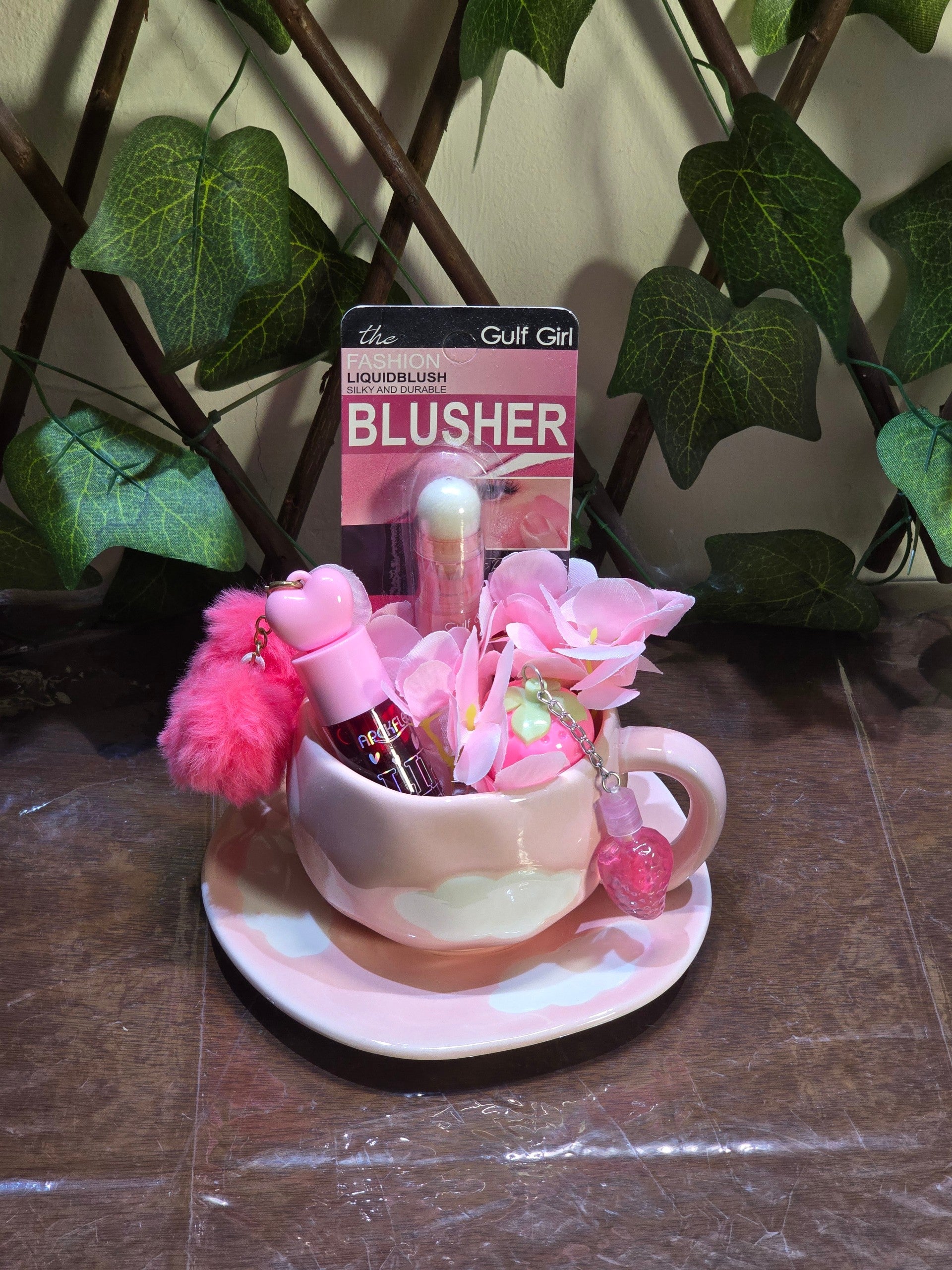 BioCode pink ceramic teacup gift set featuring liquid blusher, heart charms, and faux flowers on a wooden surface.