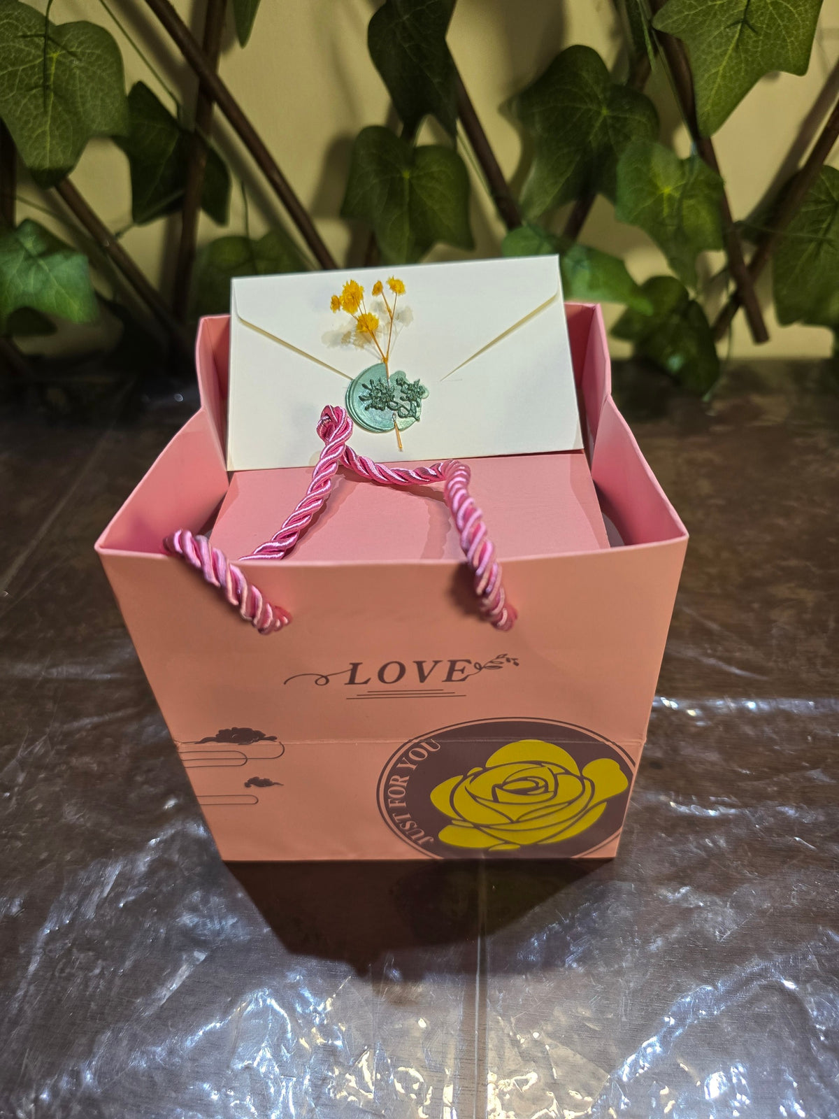 BioCode pink gift bag with rope handles, featuring a wax-sealed envelope with dried flowers for a romantic gift.