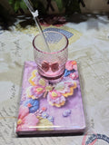 BioCode pink honeycomb glass tumbler with bow and butterfly straw resting on a floral butterfly notebook