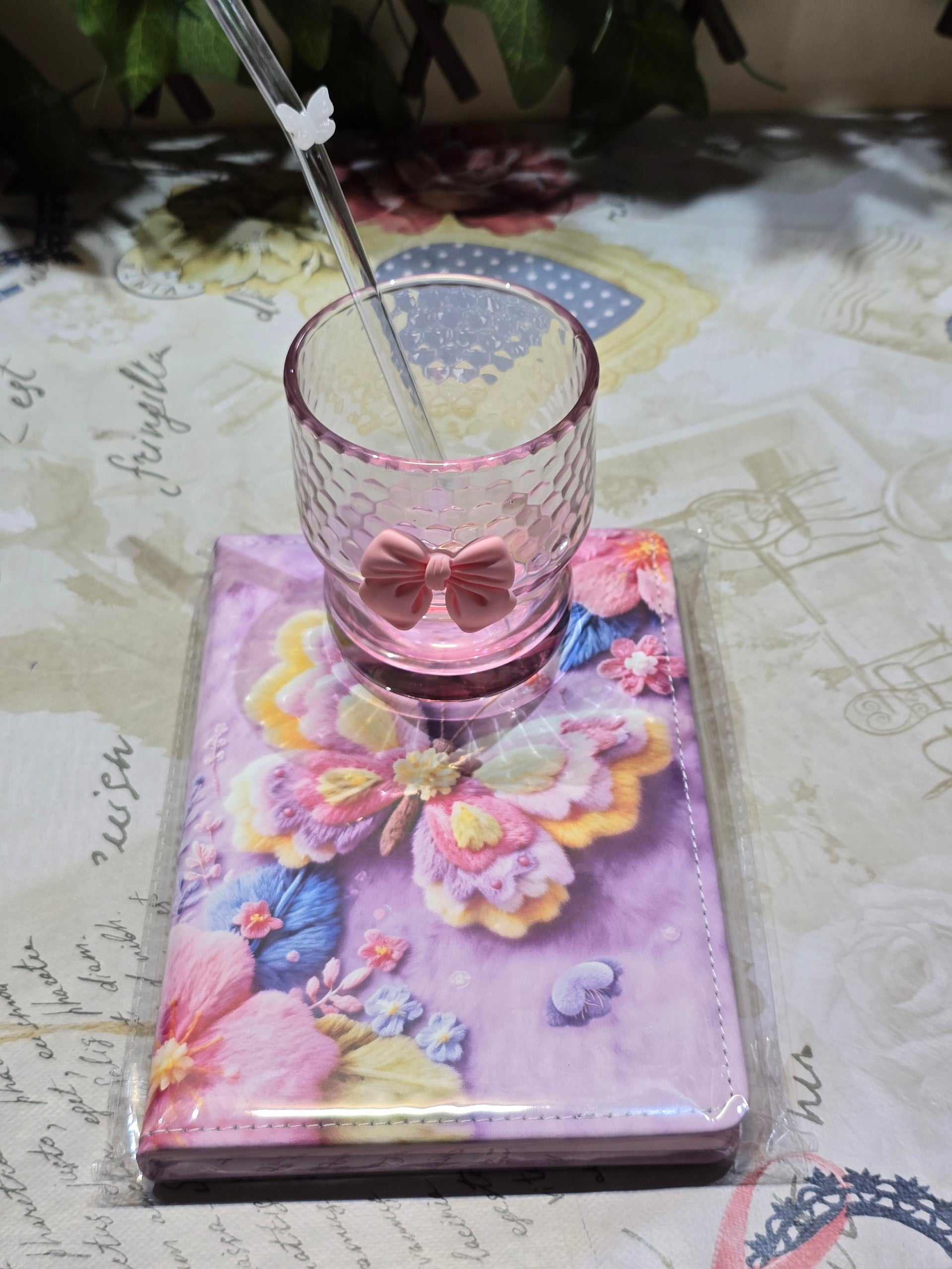 BioCode pink honeycomb glass tumbler with bow and butterfly straw resting on a floral butterfly notebook