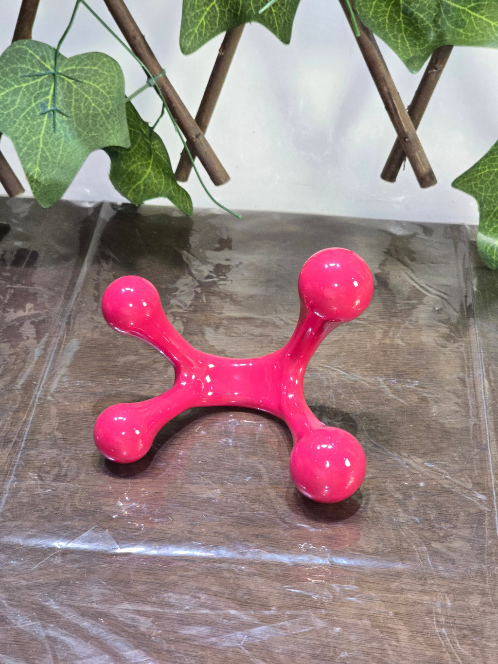 BioCode pink four-point handheld massage tool for muscle tension relief and relaxation on a wooden surface