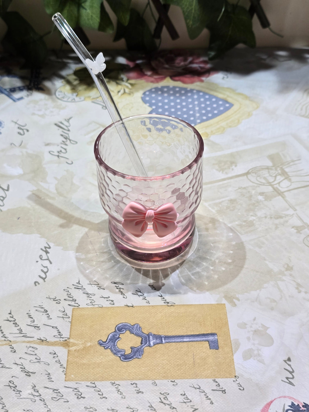 BioCode pink honeycomb glass tumbler with a raised bow and butterfly glass straw on a floral patterned surface