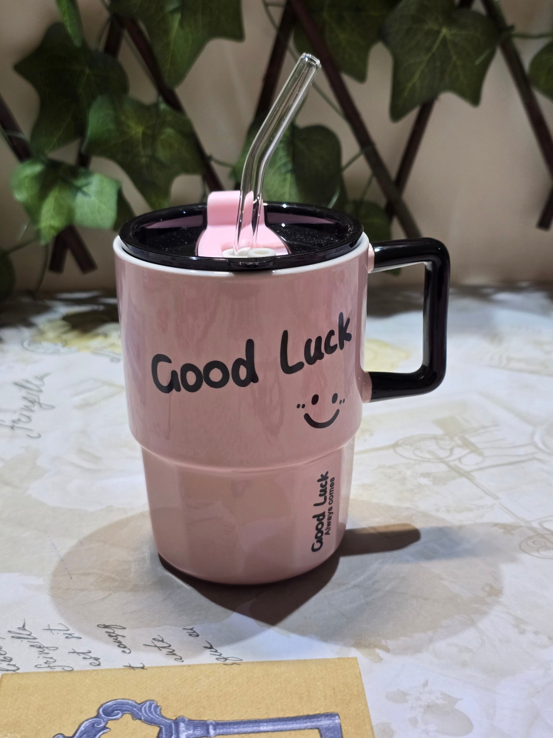 BioCode pastel pink insulated mug with a black handle, lid, glass straw, and Good Luck smiley face design.