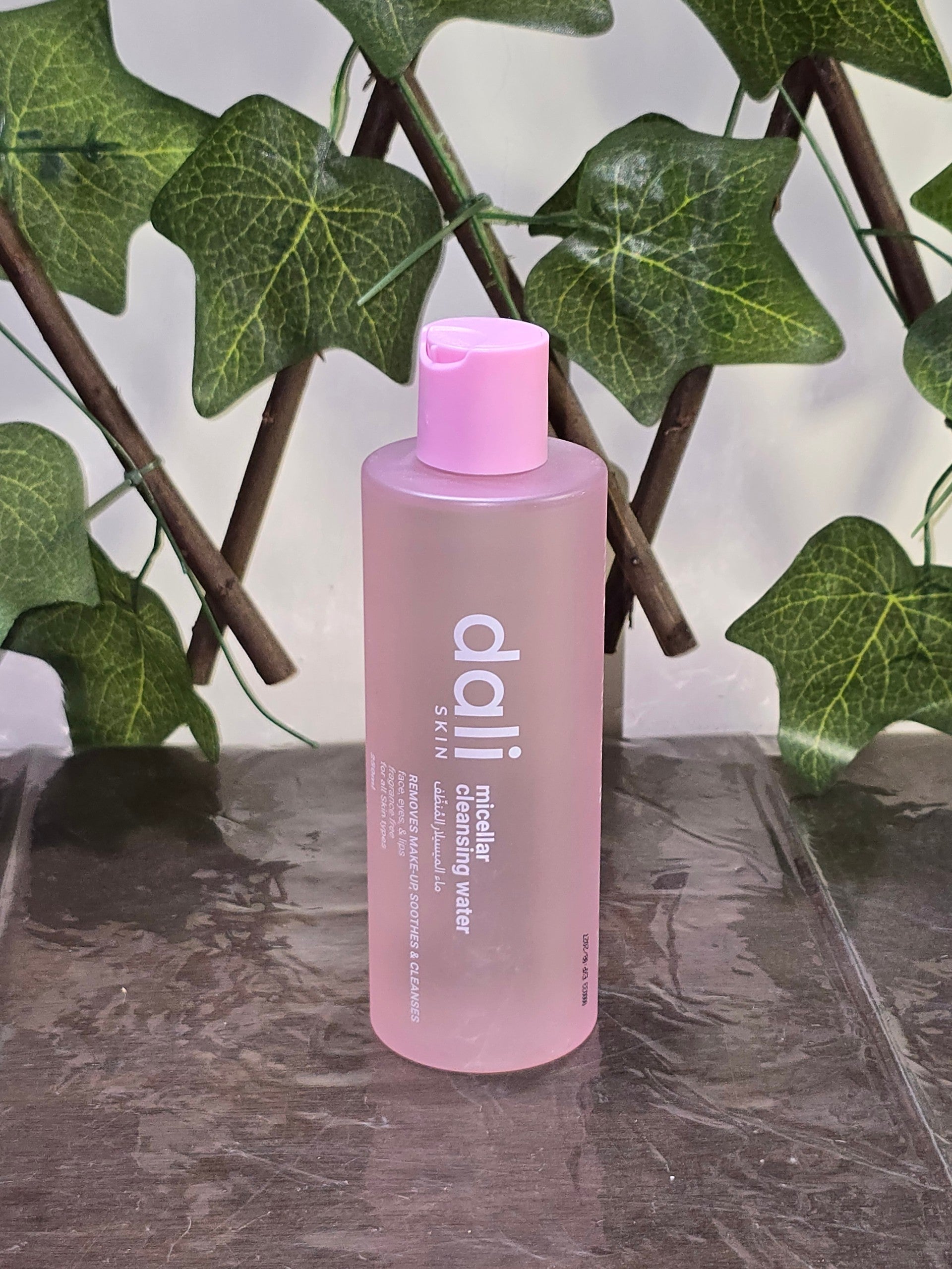 BioCode pink micellar cleansing water bottle for face and eyes, positioned in front of green ivy leaves