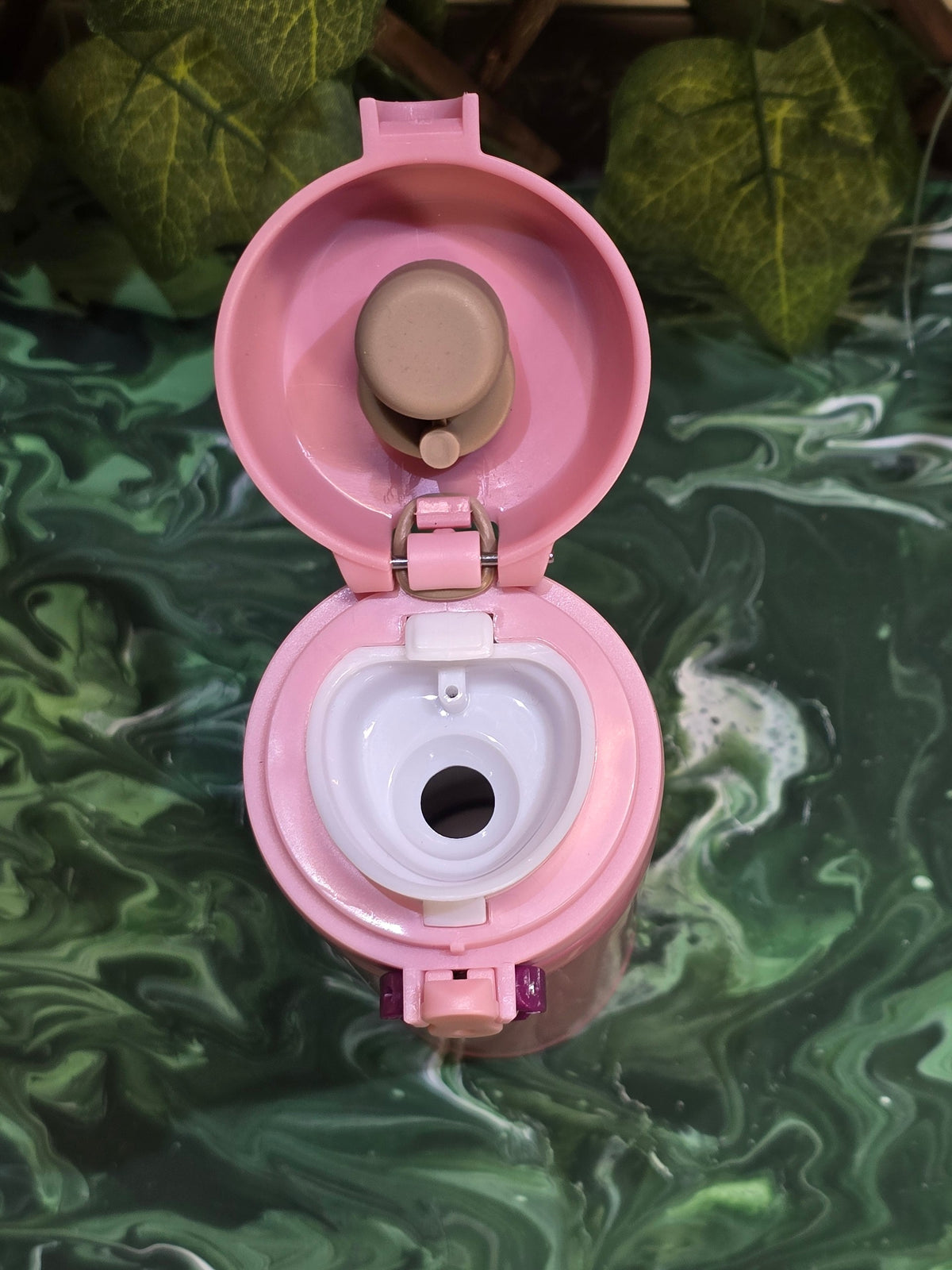 BioCode pink stainless steel travel flask with open leak-proof flip-top lid, viewed from above on a green background.