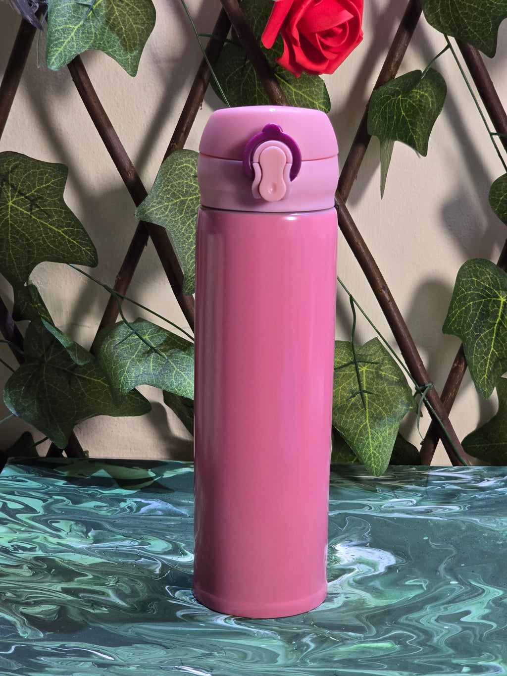 BioCode pink stainless steel insulated travel flask with a secure leak-proof flip-top lid against a garden backdrop.