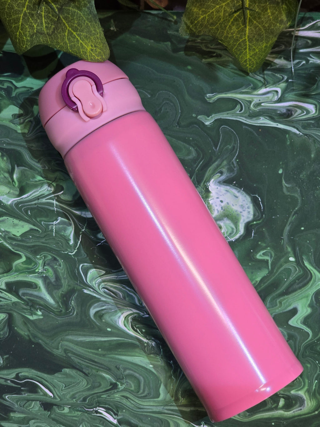 BioCode pink stainless steel vacuum insulated travel flask with a secure leak-proof flip-top lid on a green surface.