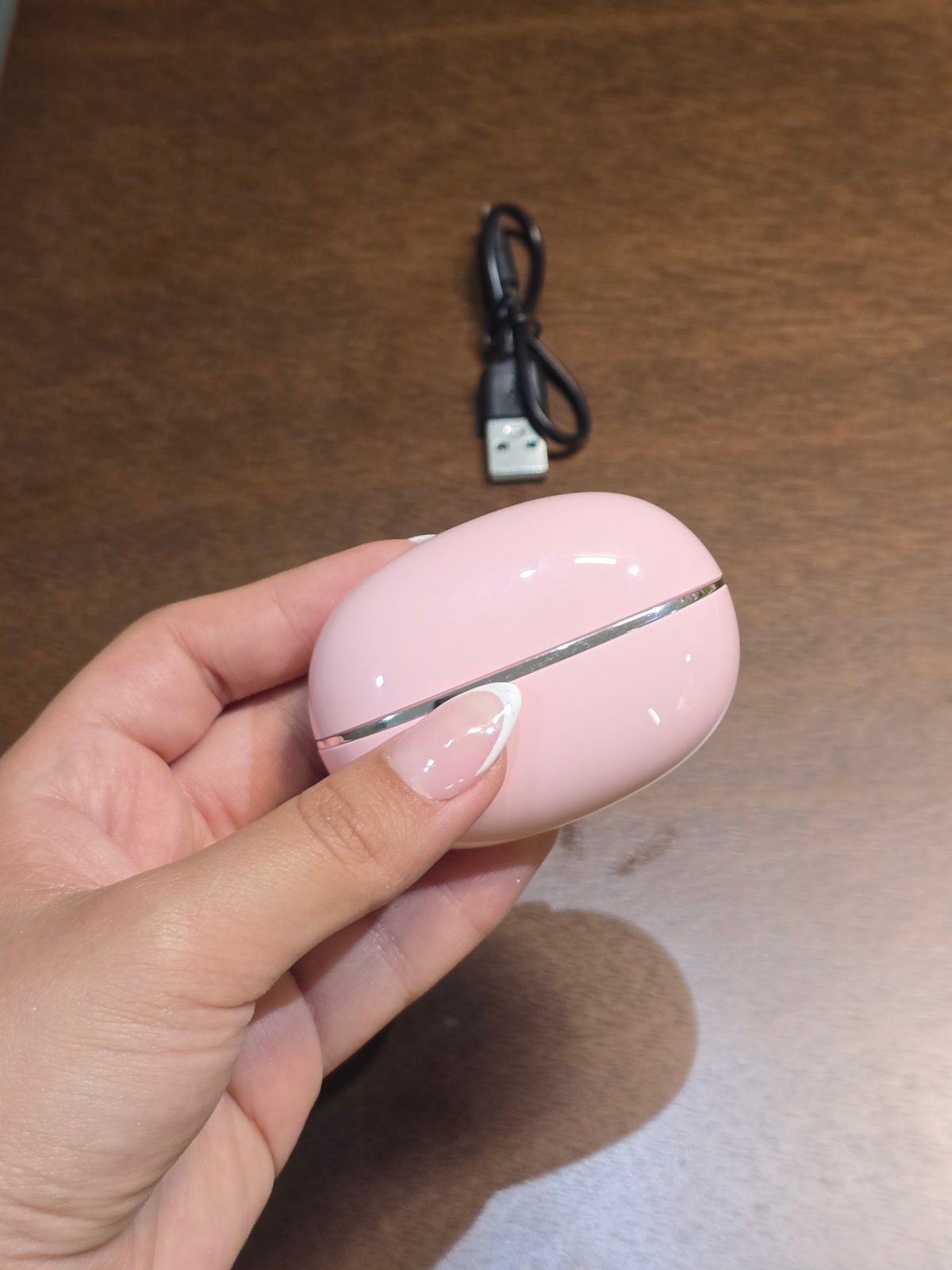 BioCode wireless earbuds in a soft pink pebble-shaped charging case with rose-gold accents held in a hand.