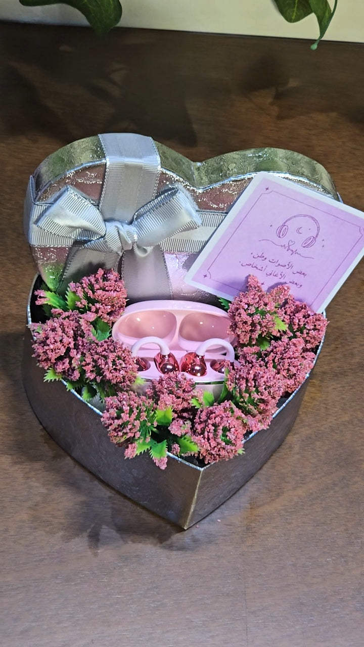 BioCode wireless earbuds in a soft pink and rose-gold finish, presented in a heart-shaped gift box with flowers.